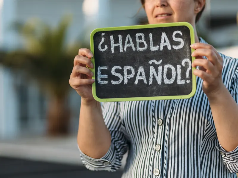 Persona sosteniendo una pizarra que dice "¿Hablas español?"